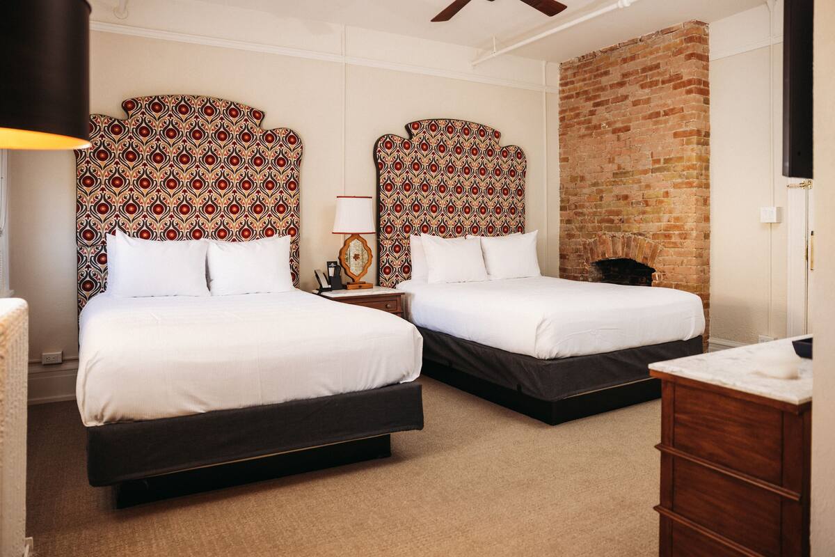 A hotel room with two beds, a brick wall, and a wooden dresser.