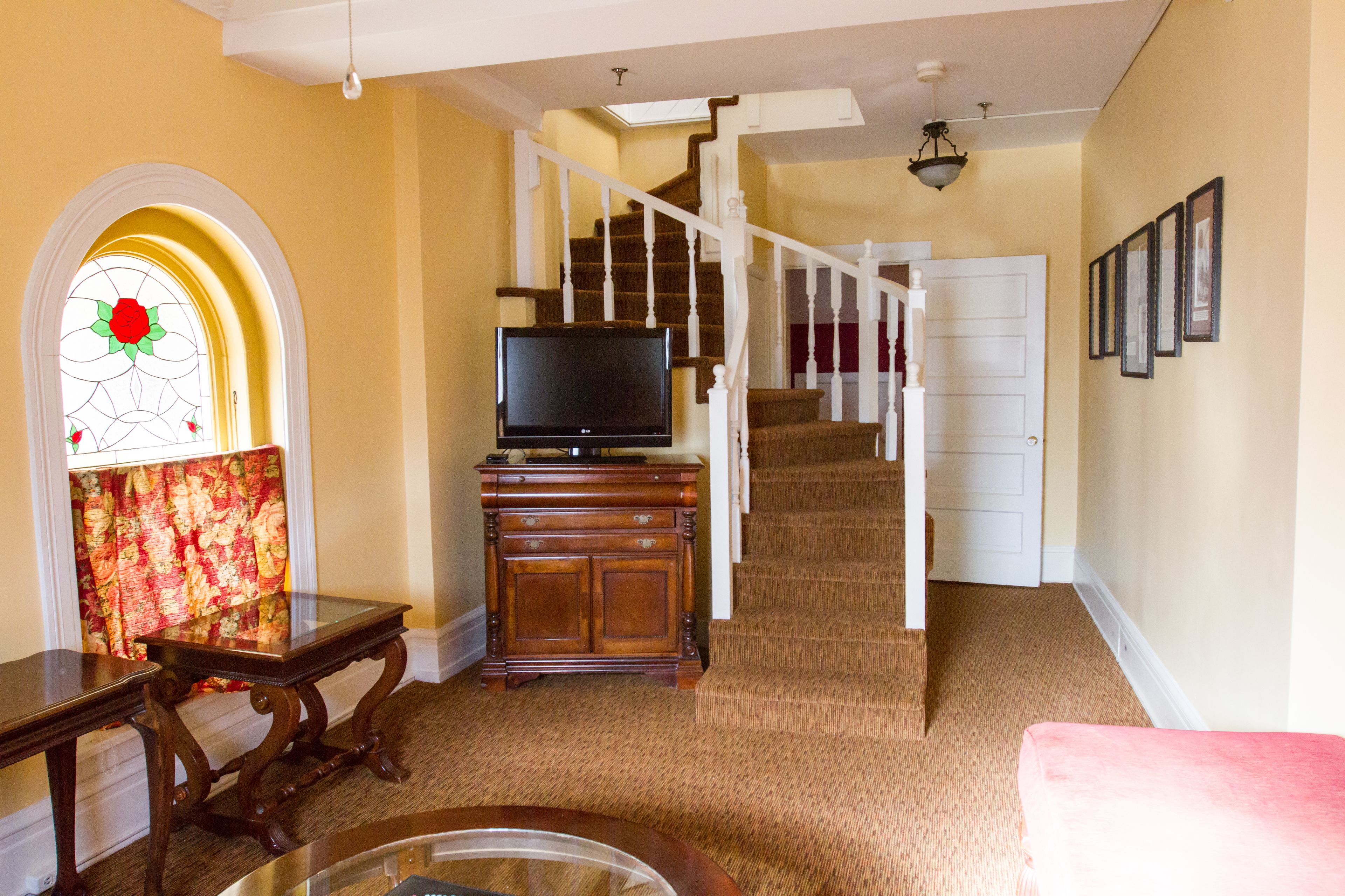 A living room with a staircase, a television on a wooden stand, a floral curtain, and a red couch.