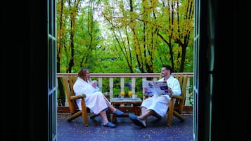 Two people sitting on wooden chairs on a wooden deck, reading a newspaper.