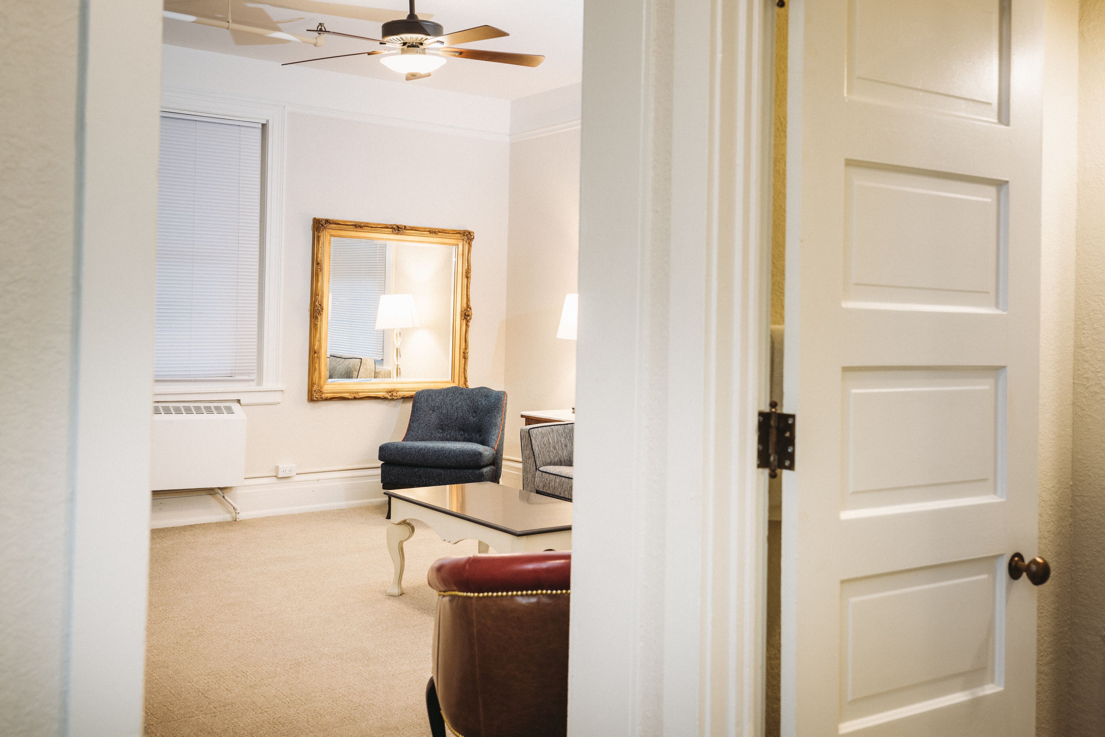 A room with a ceiling fan, a large mirror, a chair, a table, and a door.