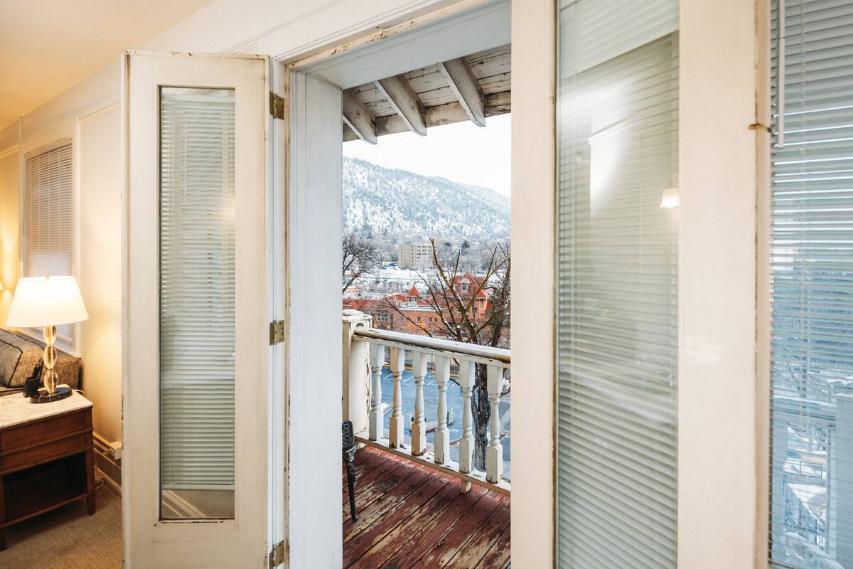 A room with a wooden floor, a white door, and a view of a snowy landscape through a window.