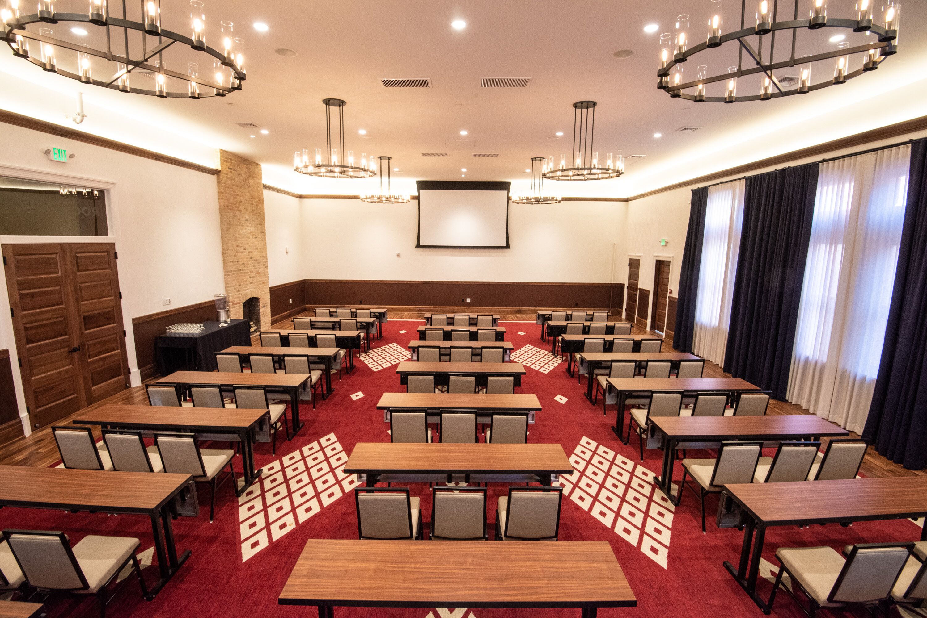 Un salón de conferencias con varias mesas y sillas, una pantalla grande y candelabros.