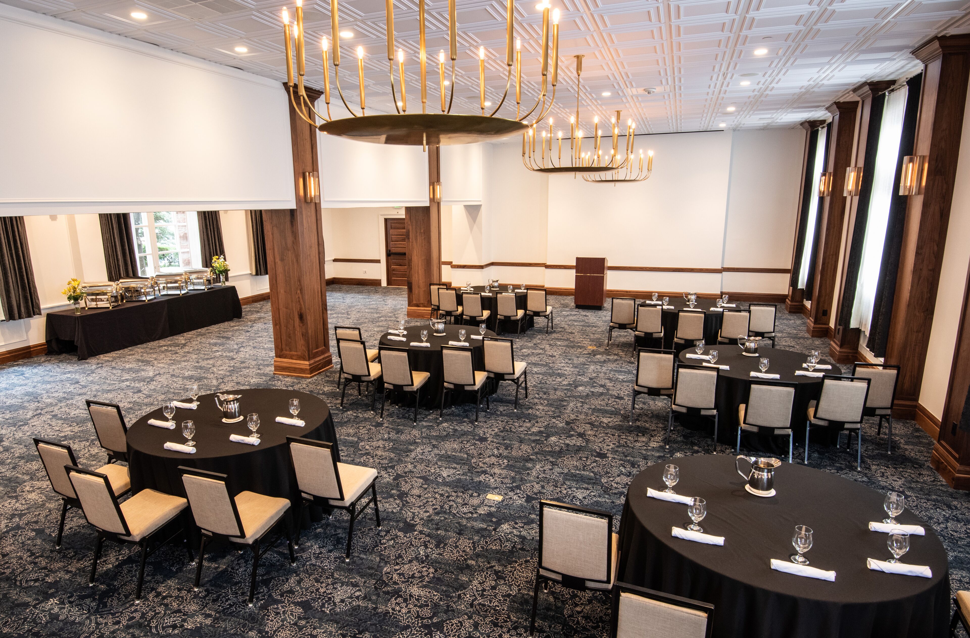 A conference room with multiple round tables, each set with chairs, glasses, and a pitcher.