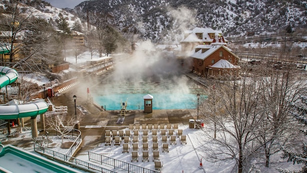 A hot spring area with a pool, seating, and a building with a snow-covered roof. - Hotel Colorado (Glenwood Springs)