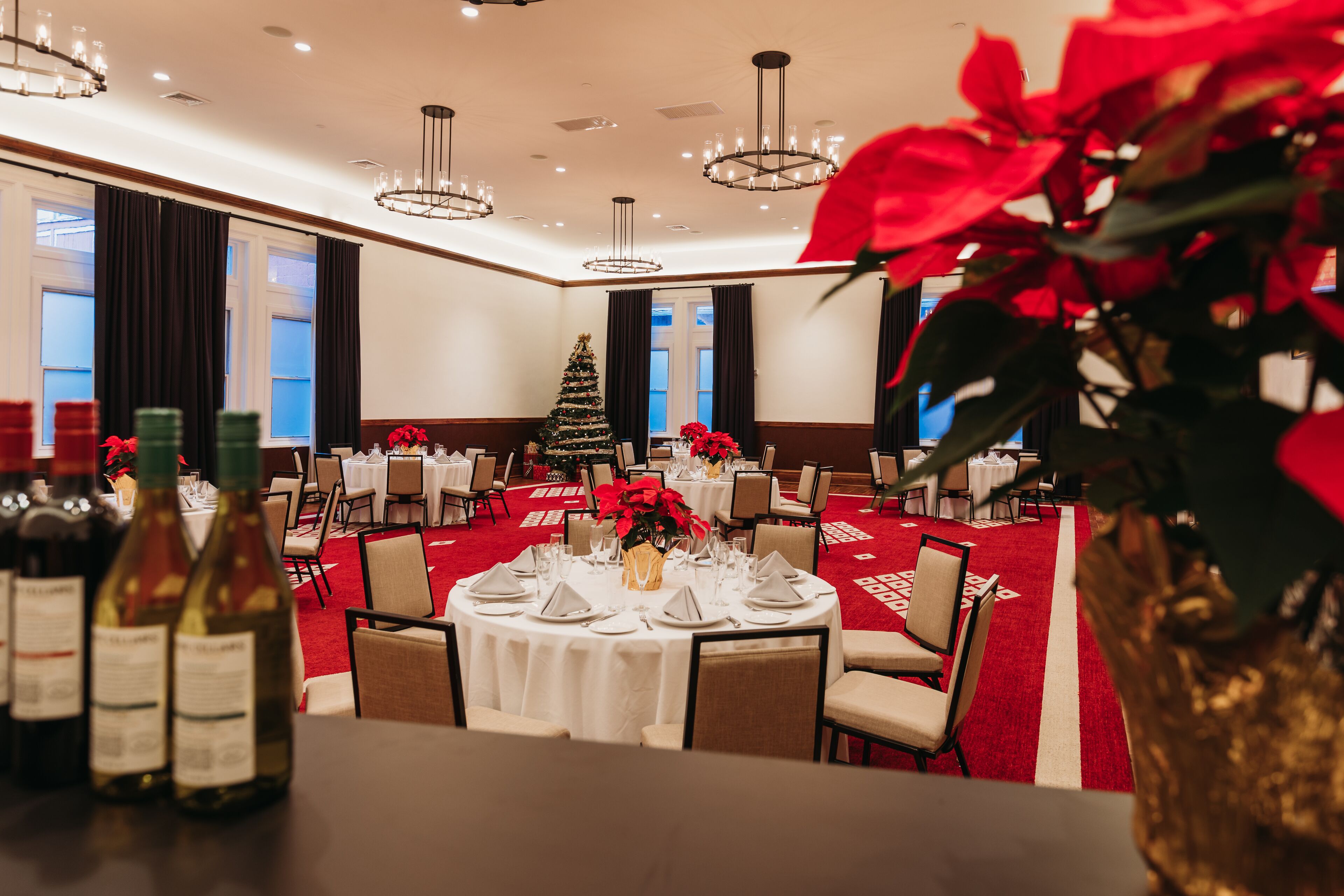 A hotel dining area with round tables set for a meal, a Christmas tree, and a red carpet.