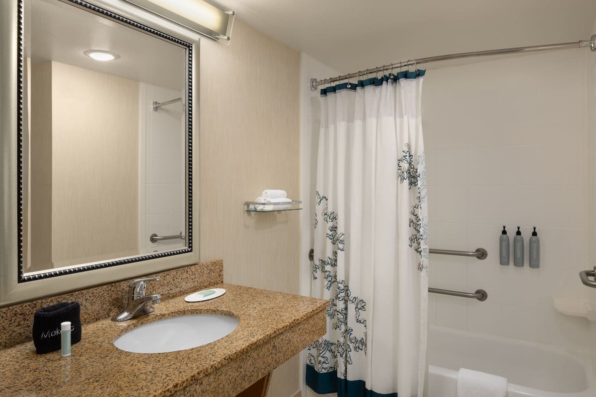 A bathroom with a granite countertop sink, a large mirror, a shower with a blue and white curtain, and a bathtub.