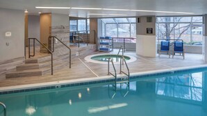 An indoor swimming pool with a clear view of the pool area, a set of stairs leading to the pool, and a seating area with chairs.