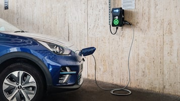 A blue car parked at an electric charging station with a parking notice sign on the wall.
