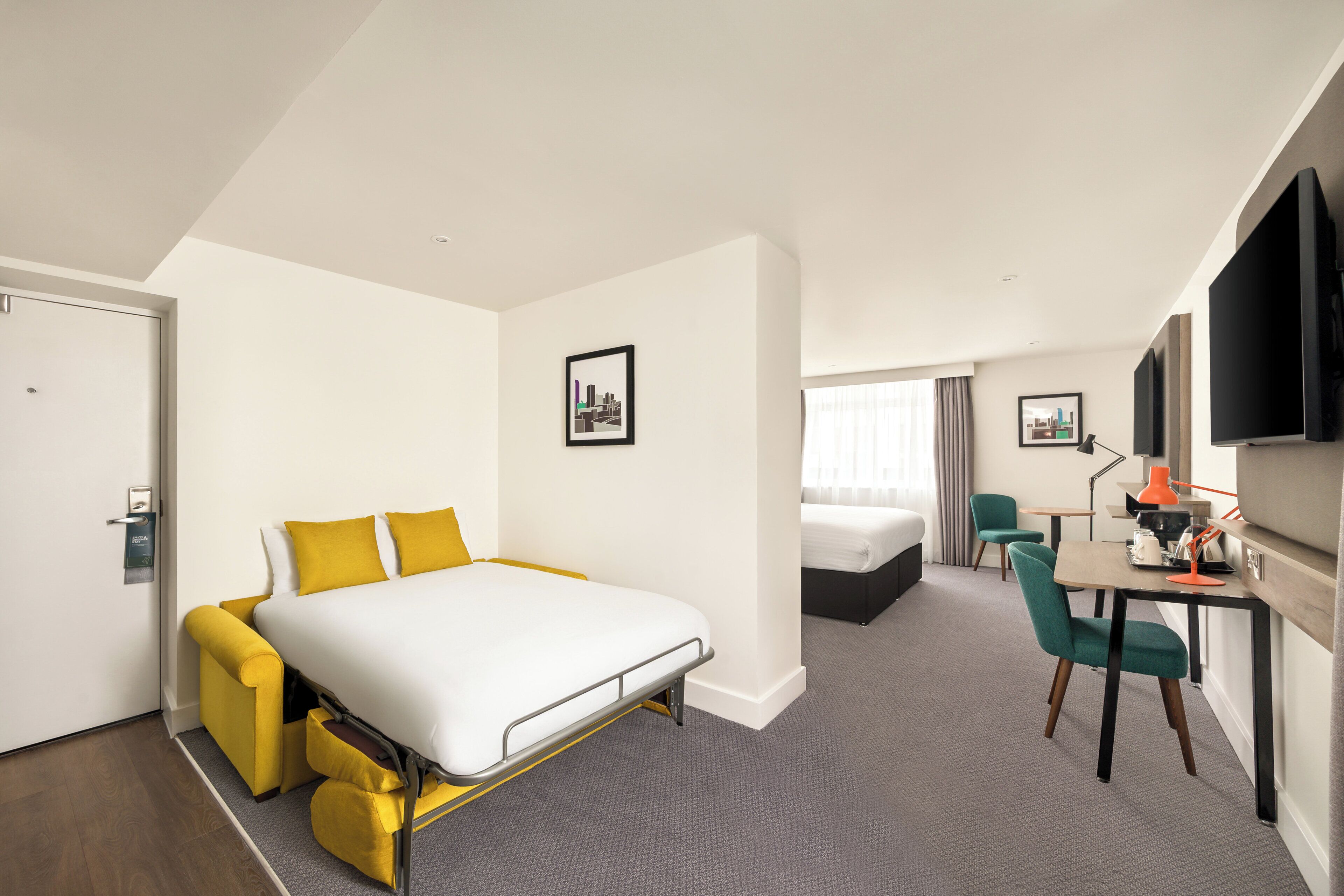 A hotel room with a bed, a desk, a chair, a TV, and a door.