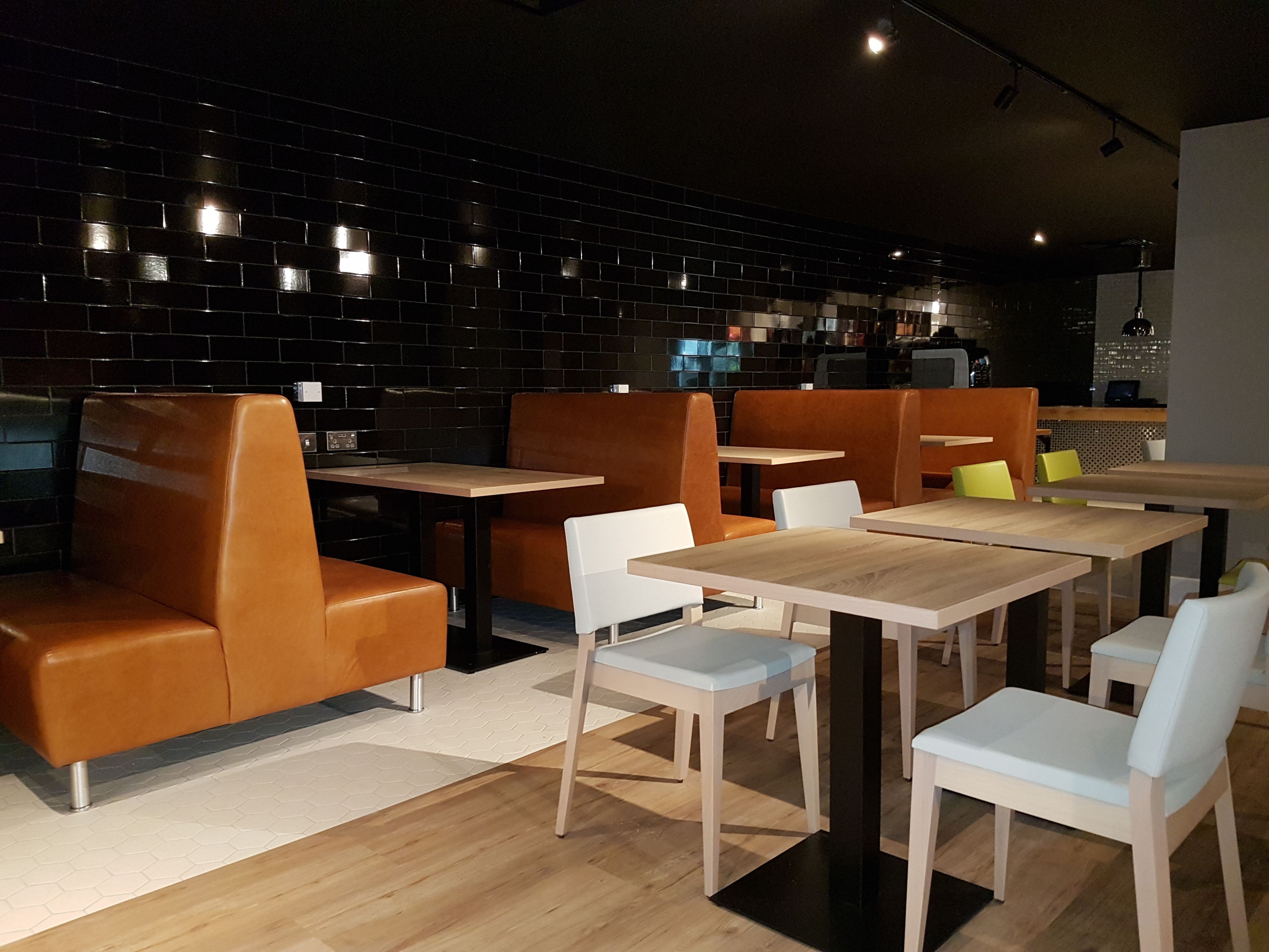 A modern restaurant interior with black tiled walls, wooden tables, and leather booths.