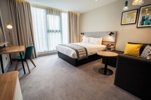 A modern hotel room with a bed, a desk, a chair, a sofa, and a small table. - Holiday Inn Birmingham City Centre by IHG (Birmingham)