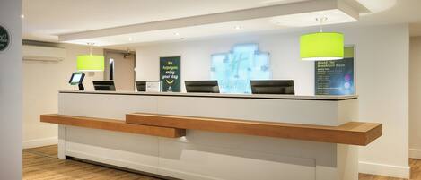 A reception desk with a digital screen, wooden counter, and green pendant lights.