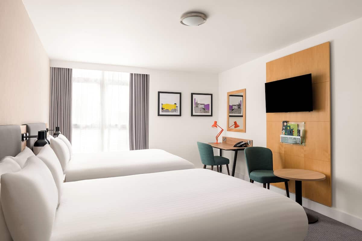 A hotel room with two beds, a desk, a chair, a TV, and artwork on the walls.