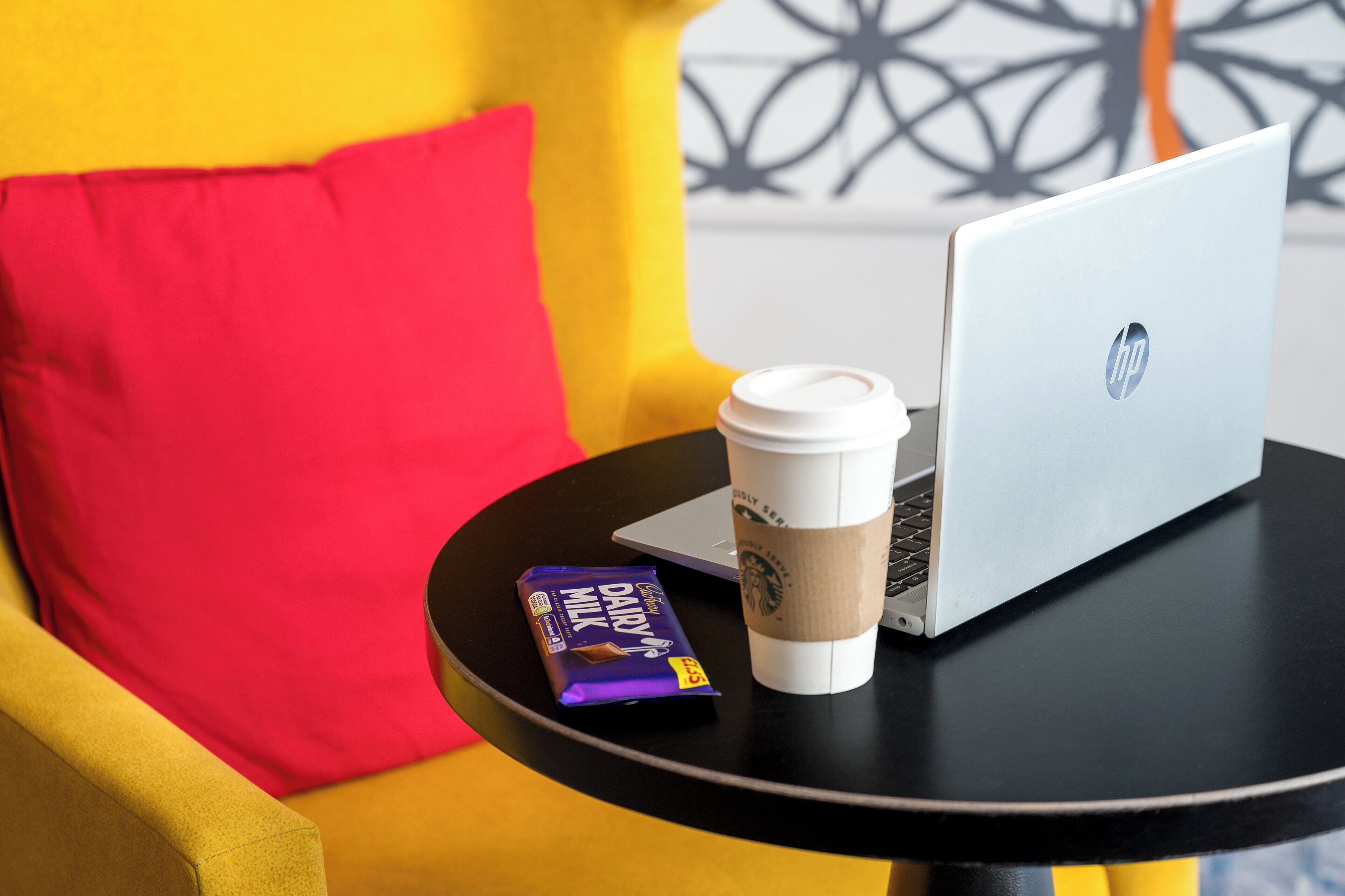 A laptop, a coffee cup, and a chocolate bar on a small table.