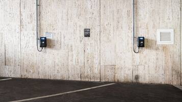 Un garaje para estacionar con piso y paredes de concreto, equipado con estaciones de carga para vehículos eléctricos y un sistema de ventilación.
