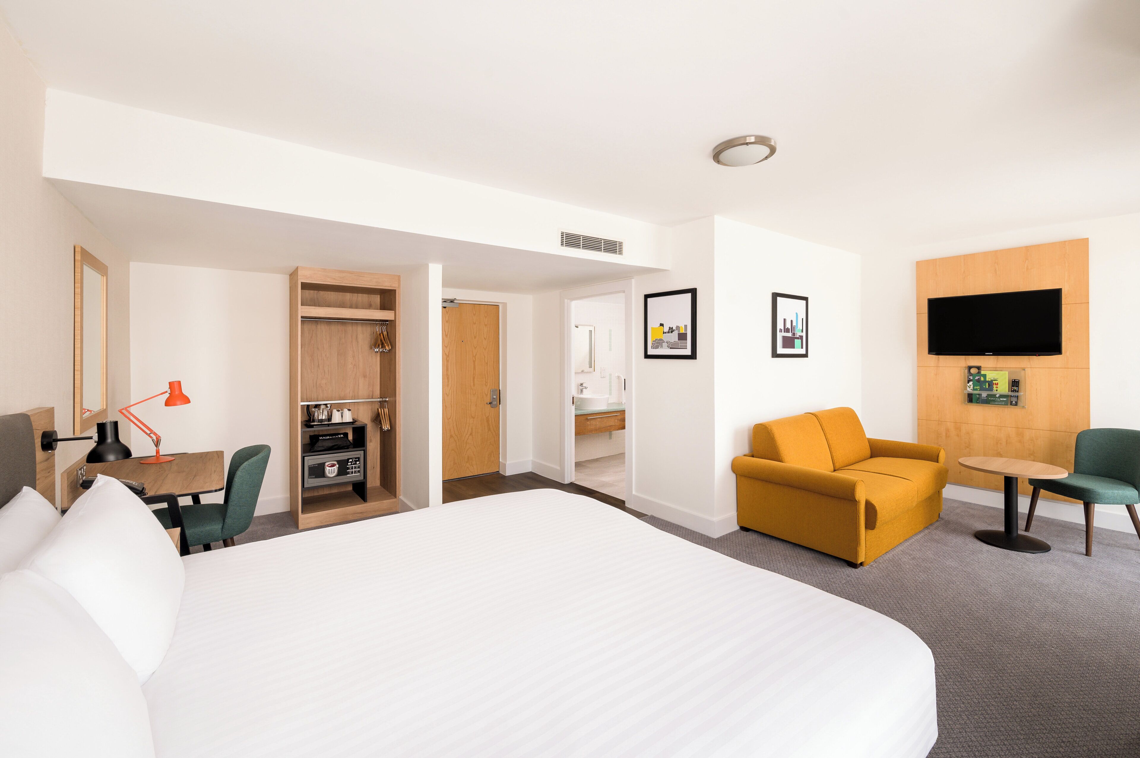A hotel room with a large bed, a desk with a chair, a sofa, a TV, and a small table.