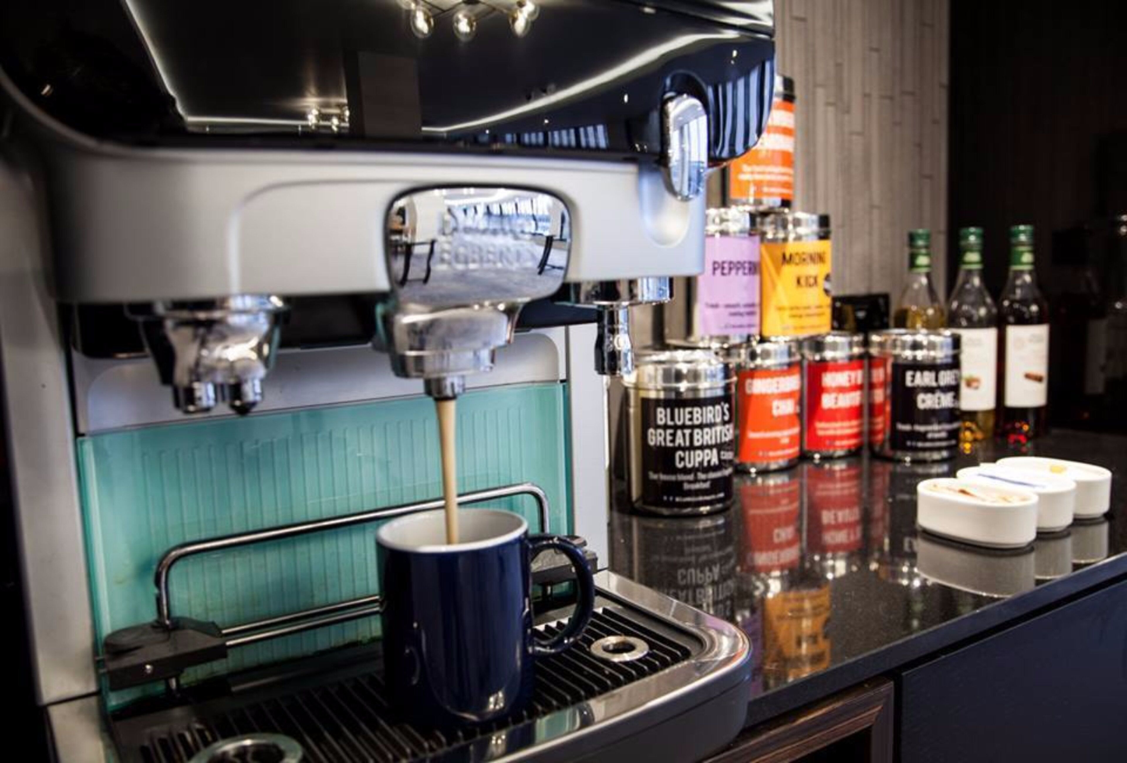 Una macchina da caffè che eroga caffè in una tazza, con diversi condimenti e salse sul bancone.