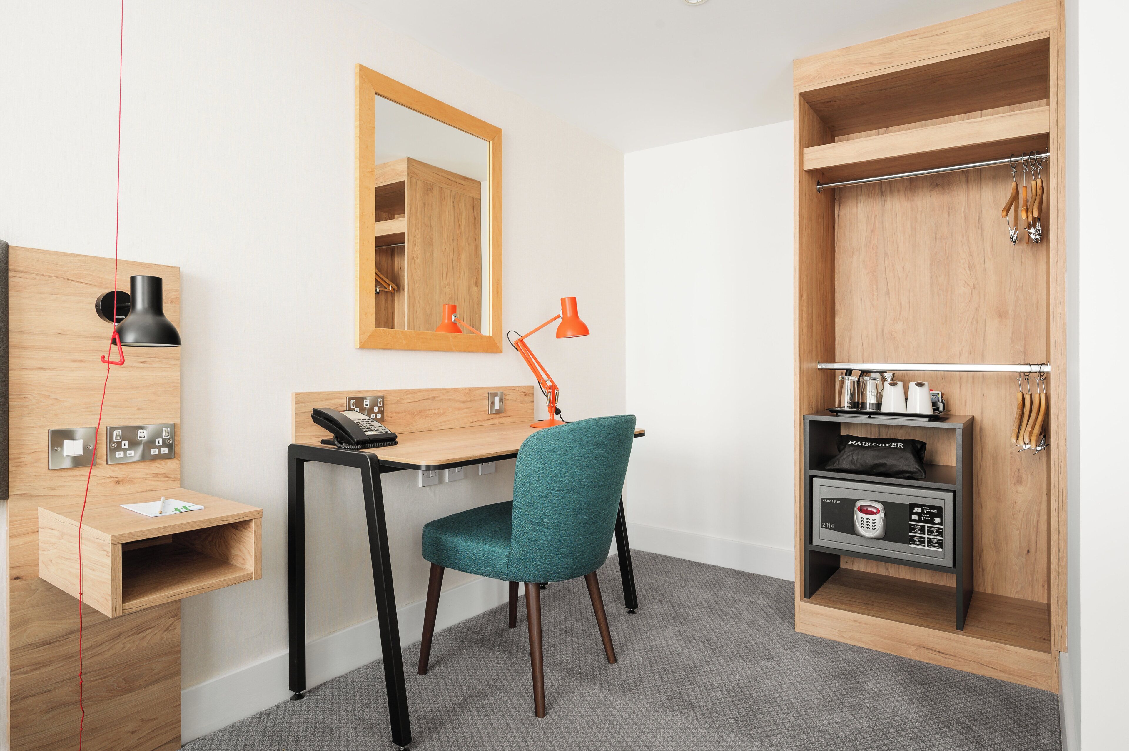 A modern room with a desk, teal chair, wooden wardrobe, and a mirror.