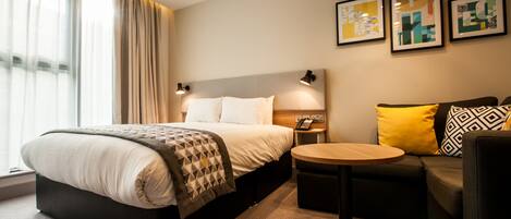 A modern hotel room with a large bed, a round table, a sofa, and artwork on the walls.