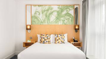 A hotel room with a large bed, two bedside tables, a telephone, and a mirror with a green abstract painting.