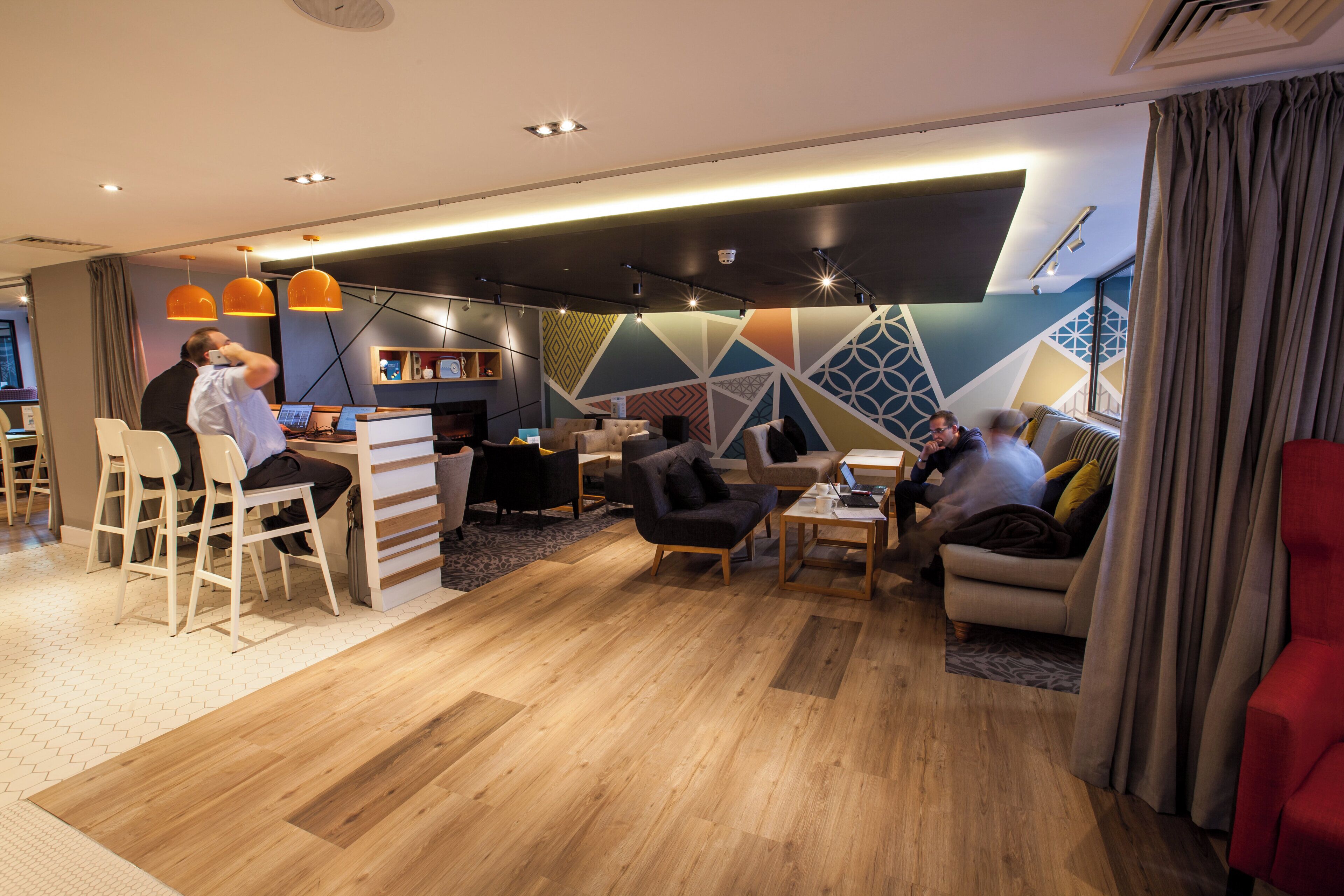 A modern hotel lobby with a reception desk, seating area, and a bar.