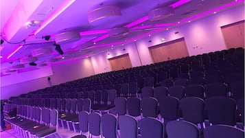 An auditorium with rows of chairs, ceiling lights, and a projector.