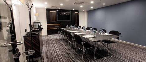 A conference room with a long table, chairs, a coffee machine, and a TV screen.