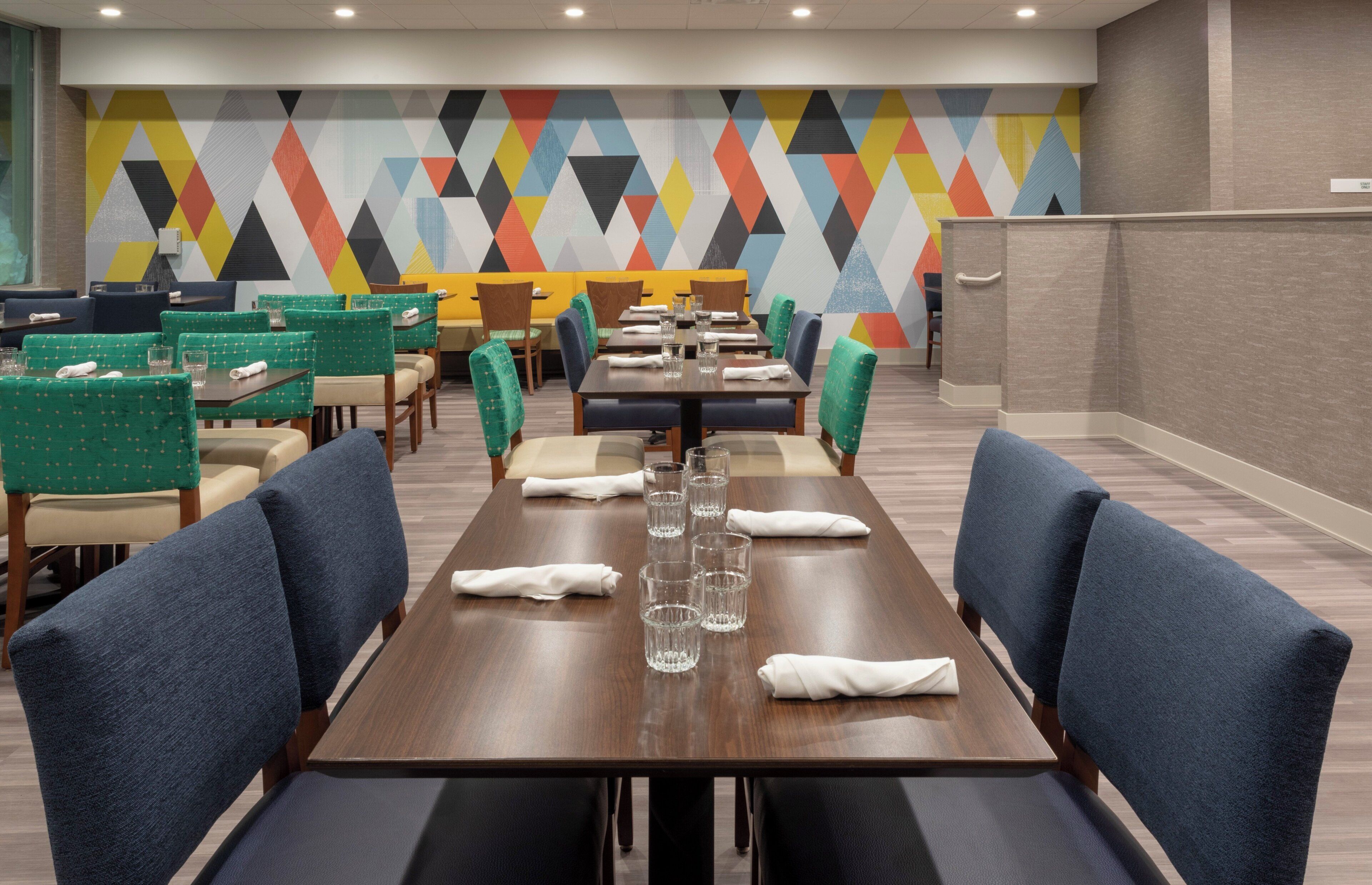 A hotel dining area with multiple tables and chairs, a colorful geometric wall design, and a 'STAFF ONLY' sign on the wall.