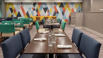 A hotel dining area with multiple tables and chairs, a colorful geometric wall design, and a 'STAFF ONLY' sign on the wall.