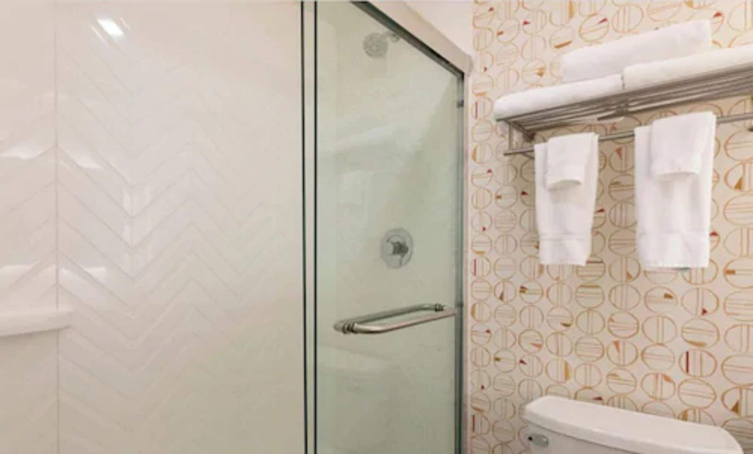 Casa de banho com chuveiro de porta de vidro, sanita e toalheiro com toalhas.