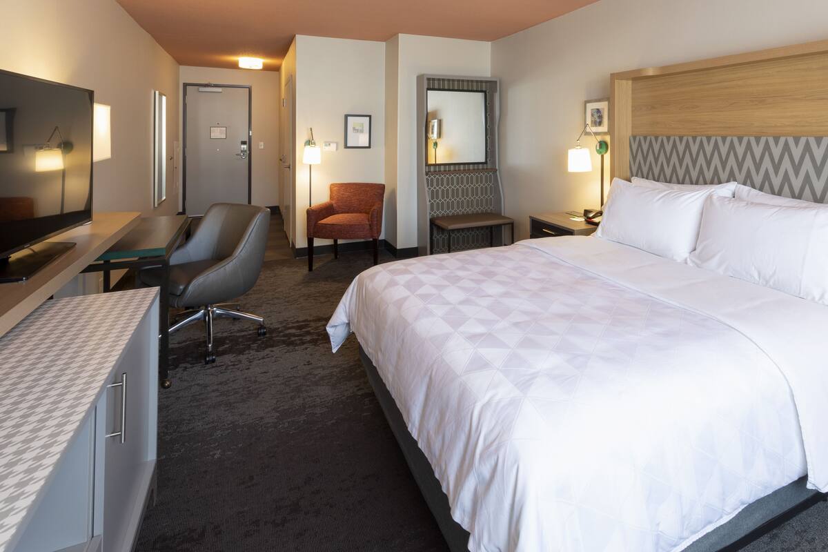 A hotel room with a large bed, a desk with a chair, a television, and a mirror.