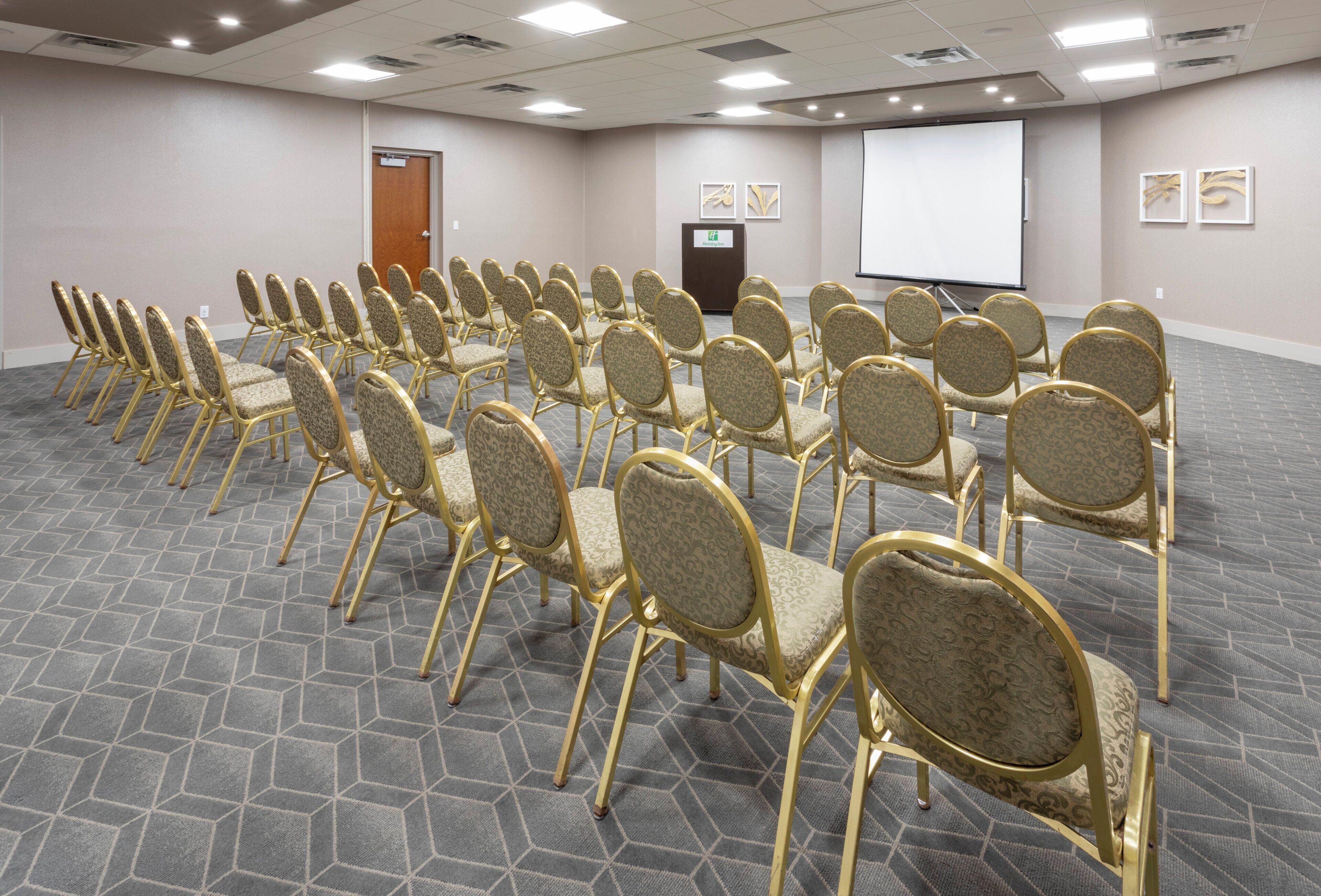 A conference room with rows of chairs, a podium, and a projector screen.