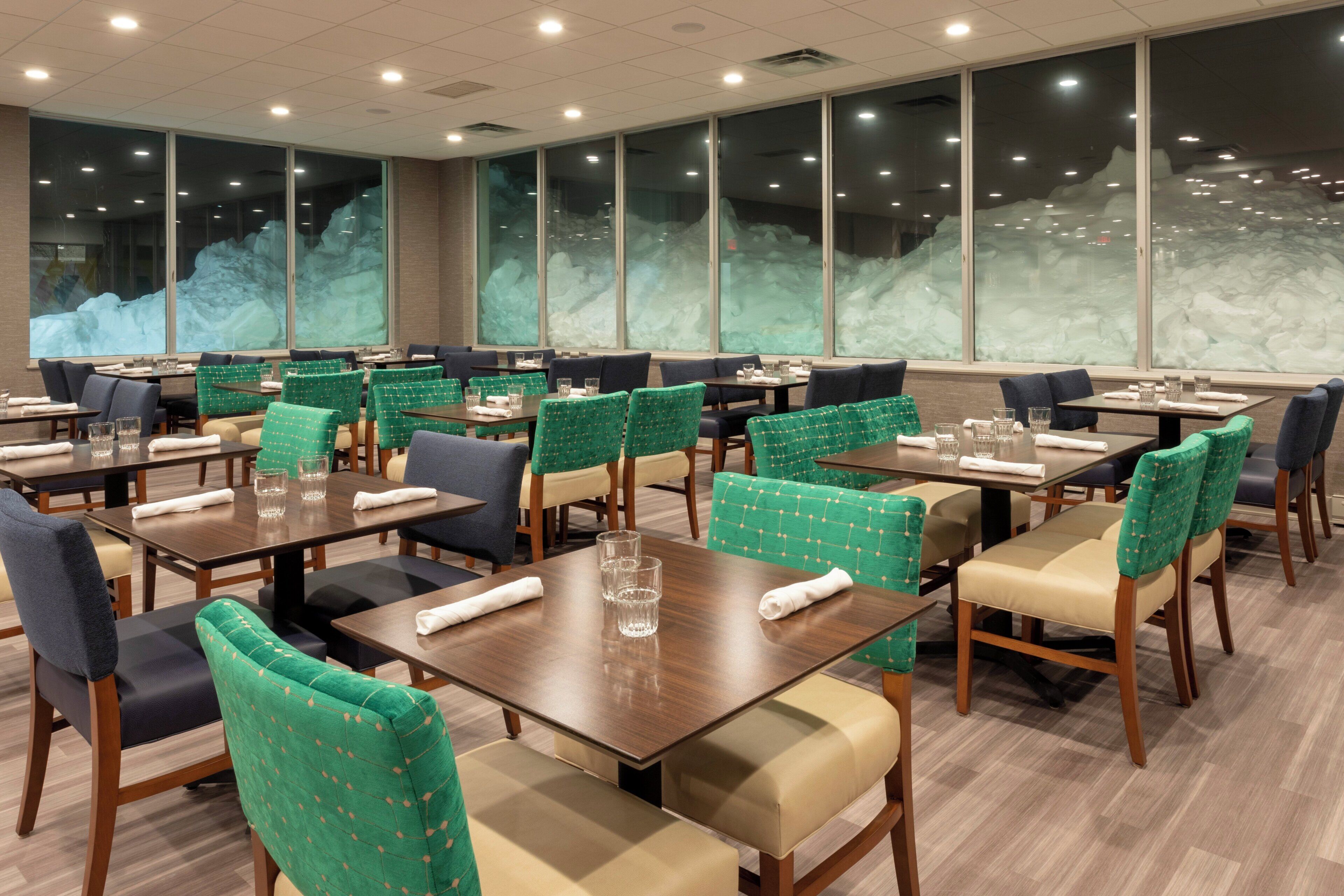 A restaurant with multiple tables and chairs, large windows with a view of a snowy landscape, and a clean, modern interior.