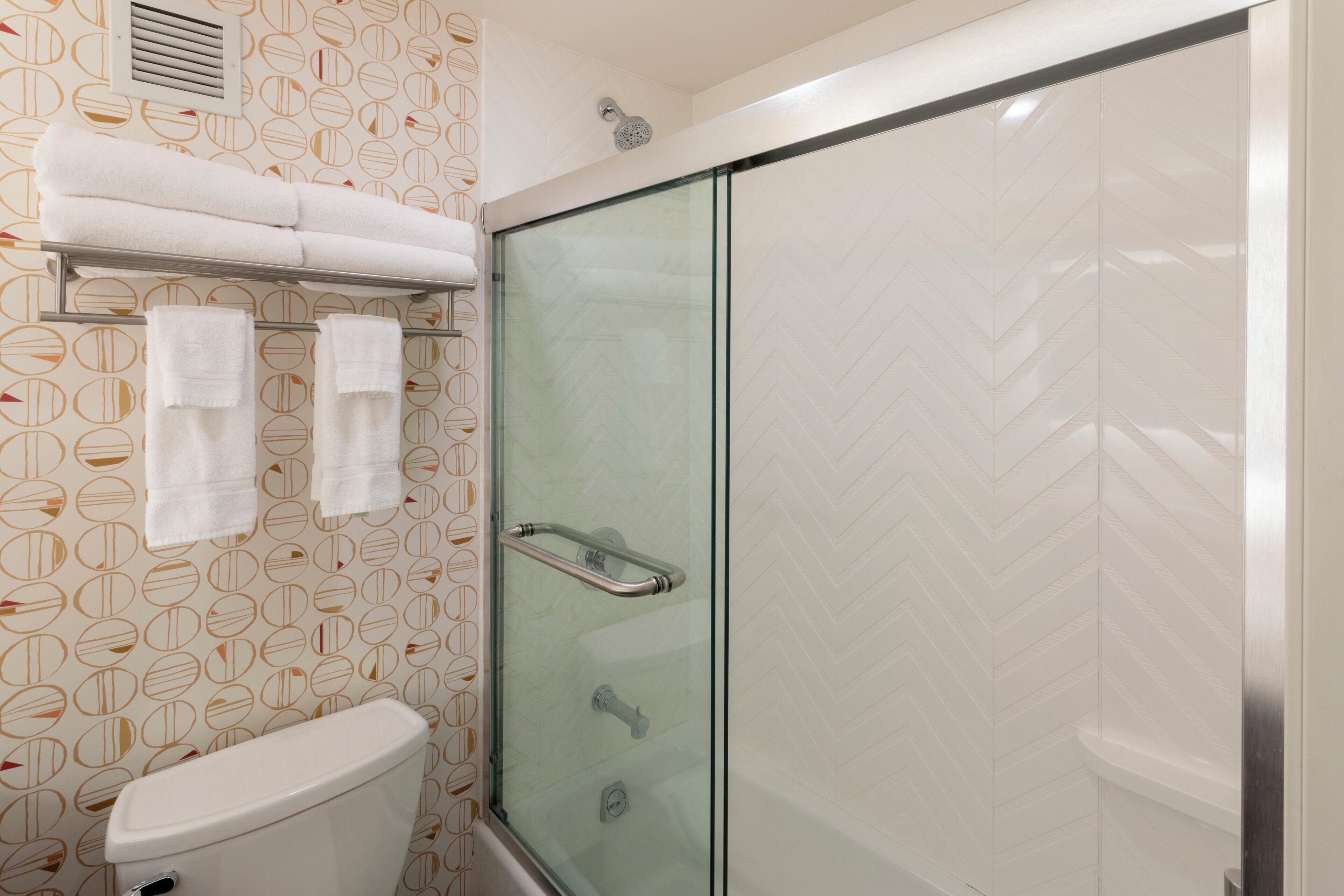 Une salle de bain avec une douche à parois de verre, des toilettes et un porte-serviettes avec plusieurs serviettes.