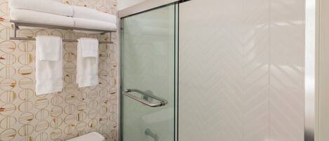 Ein Badezimmer mit Duschkabine aus Glas, Toilette und Handtuchhalter mit mehreren Handtüchern.