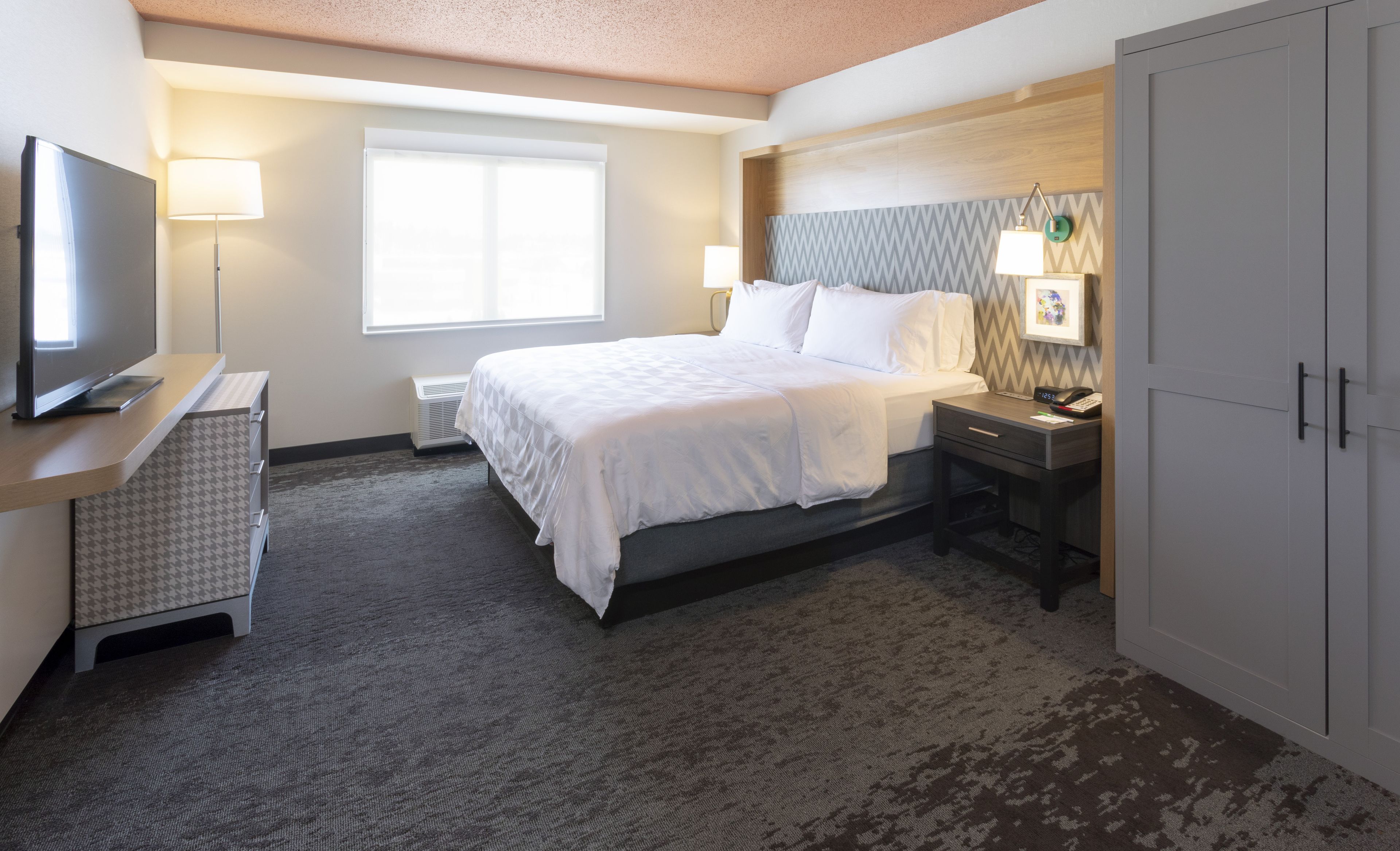 A hotel room with a bed, bedside table, lamp, TV, and wardrobe.