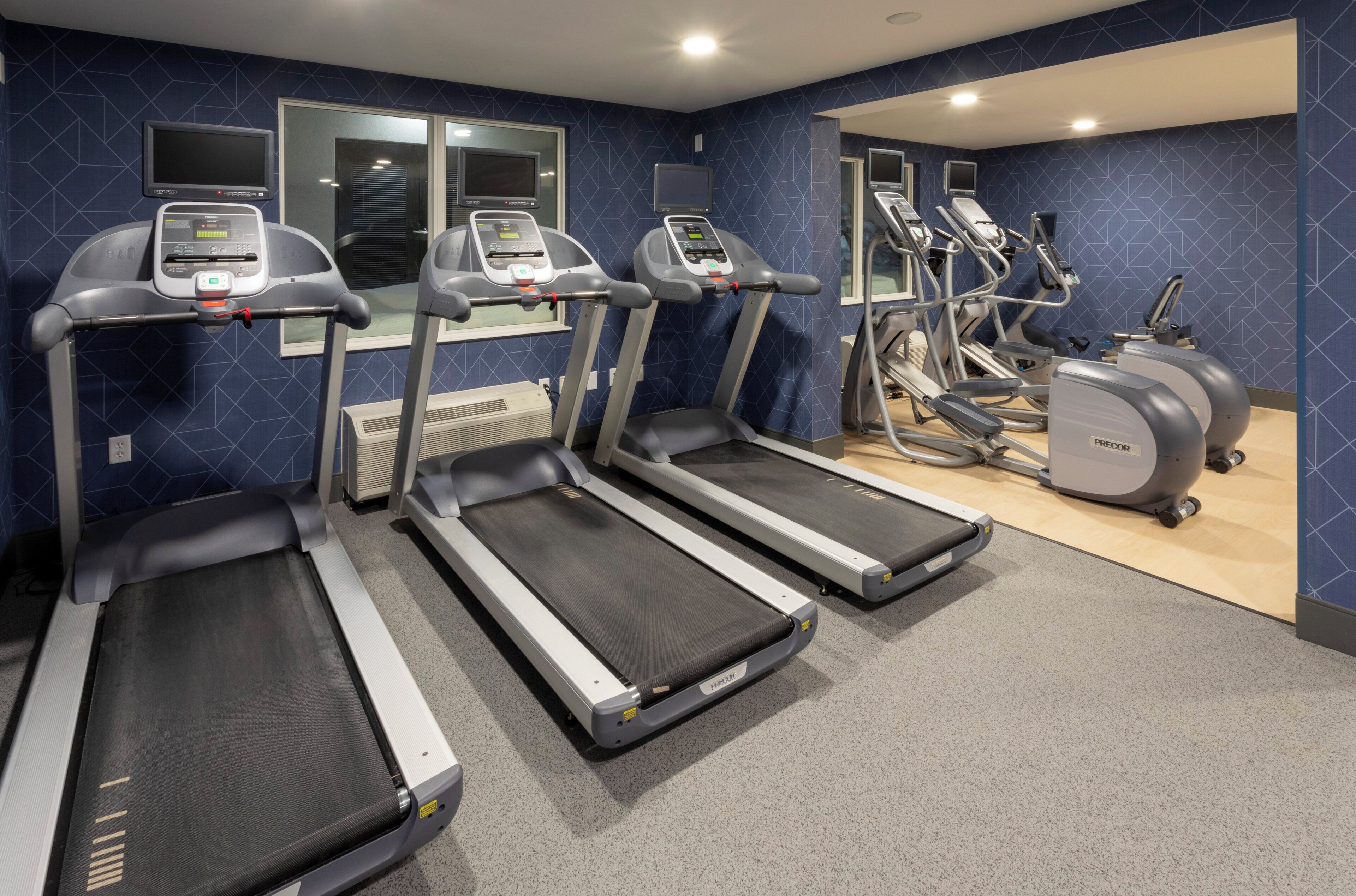 Ein Fitnessstudio mit Laufbändern, Crosstrainern und einer Spiegelwand.