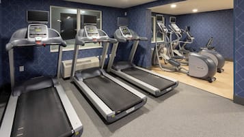 Ein Fitnessstudio mit Laufbändern, Crosstrainern und einer Spiegelwand.