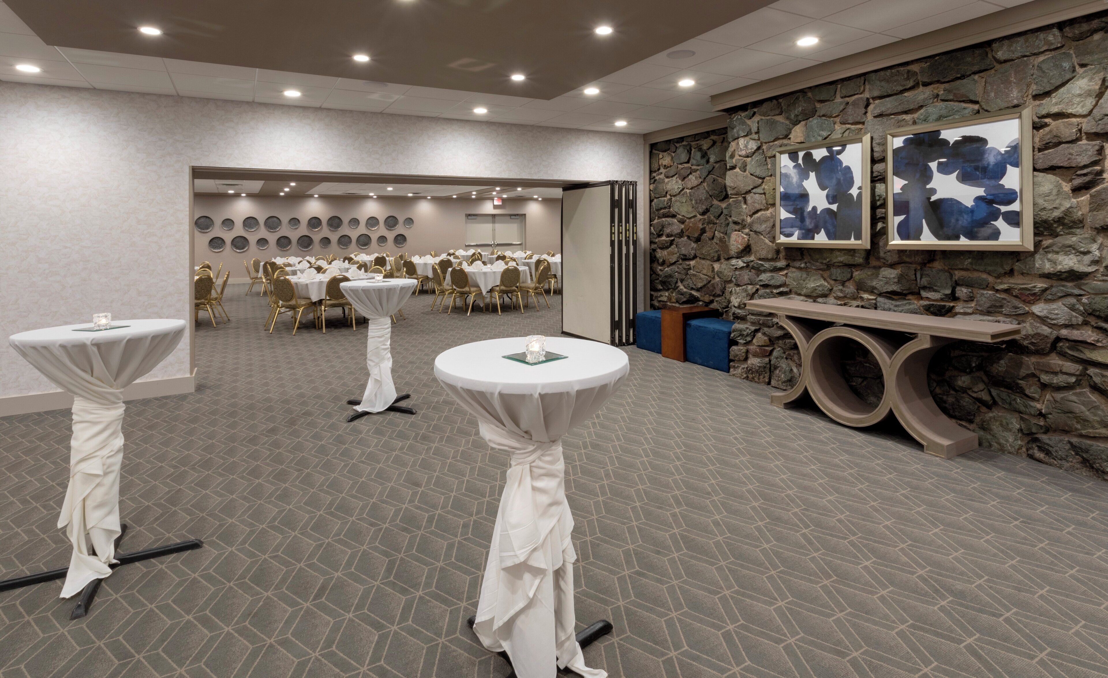 A conference room with round tables, chairs, and a stone wall with artwork.