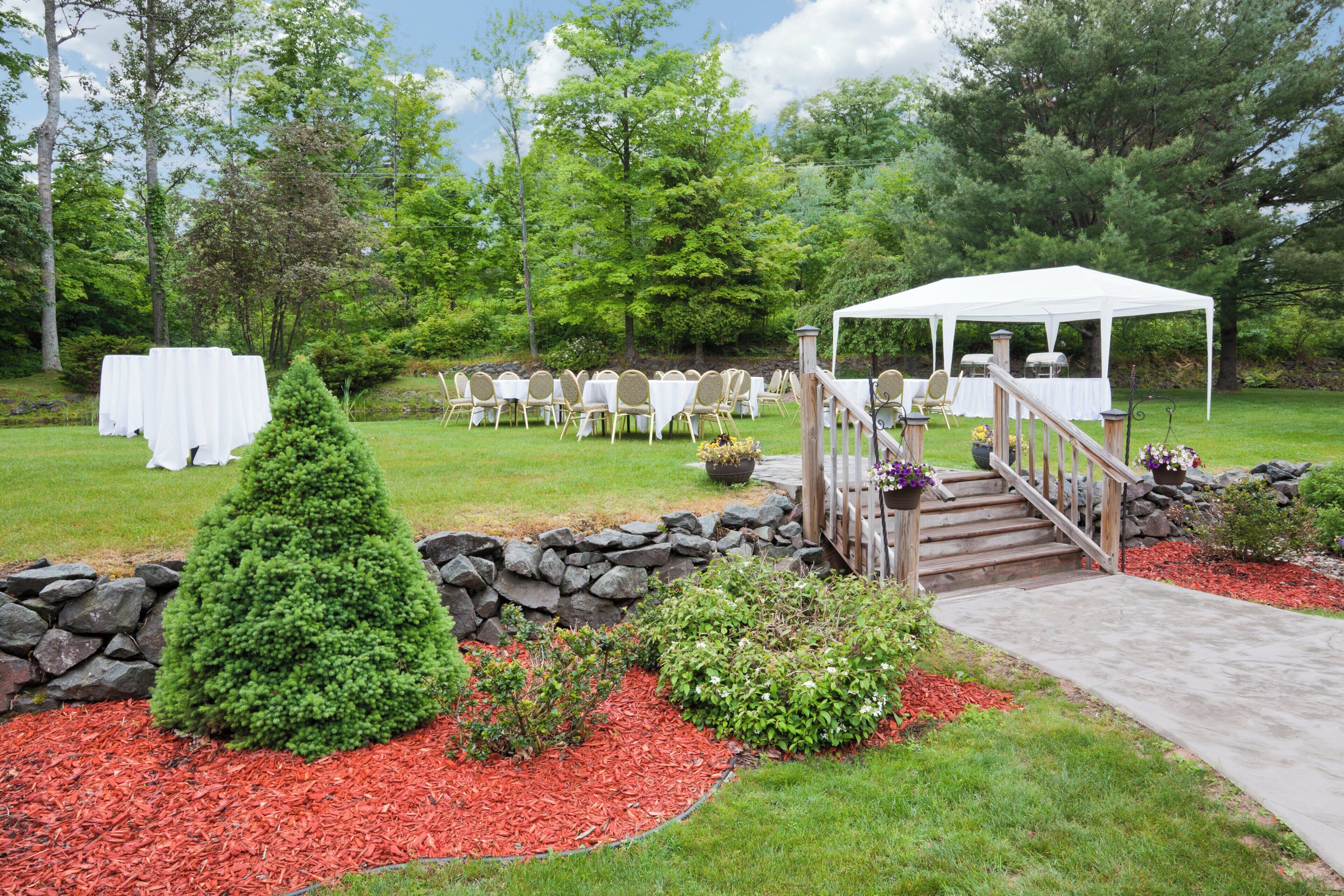 An outdoor event space with a tent, tables, chairs, and a stone wall.