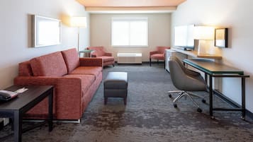 A hotel room with a red sofa, a desk with a computer, a chair, and a small table with a lamp.