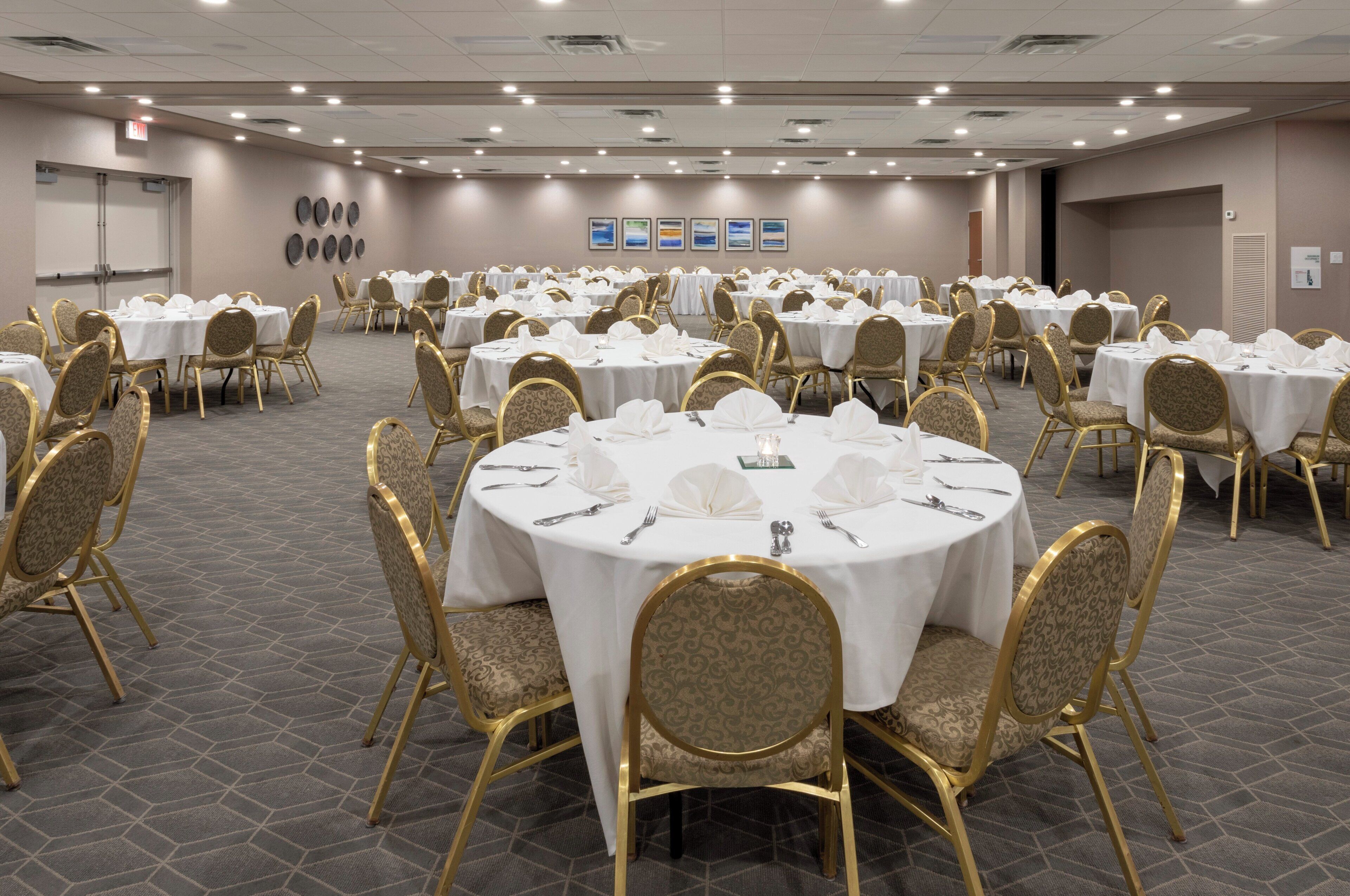 A conference room with round tables, gold chairs, and white tablecloths.