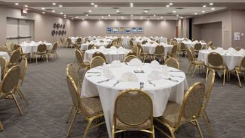 A conference room with round tables, gold chairs, and white tablecloths.