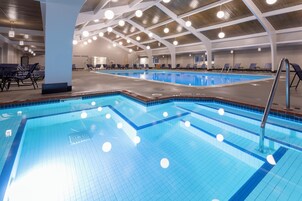 Una piscina interior con varias pistas, sillones de descanso y un techo con vigas y luminarias a la vista.