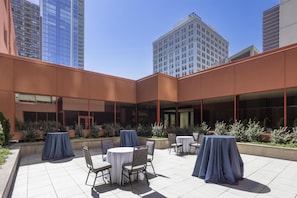 A courtyard with outdoor seating, large windows, and modern buildings in the background.