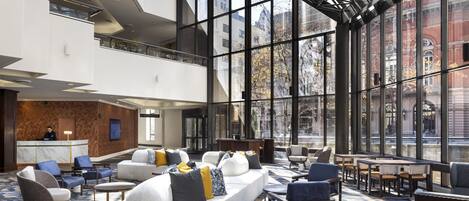 A modern hotel lobby with a high ceiling, large windows, and a seating area with sofas and chairs.
