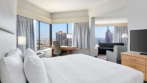 Une chambre d’hôtel avec un grand lit, un bureau, une chaise, une télévision et une vue sur le paysage urbain.