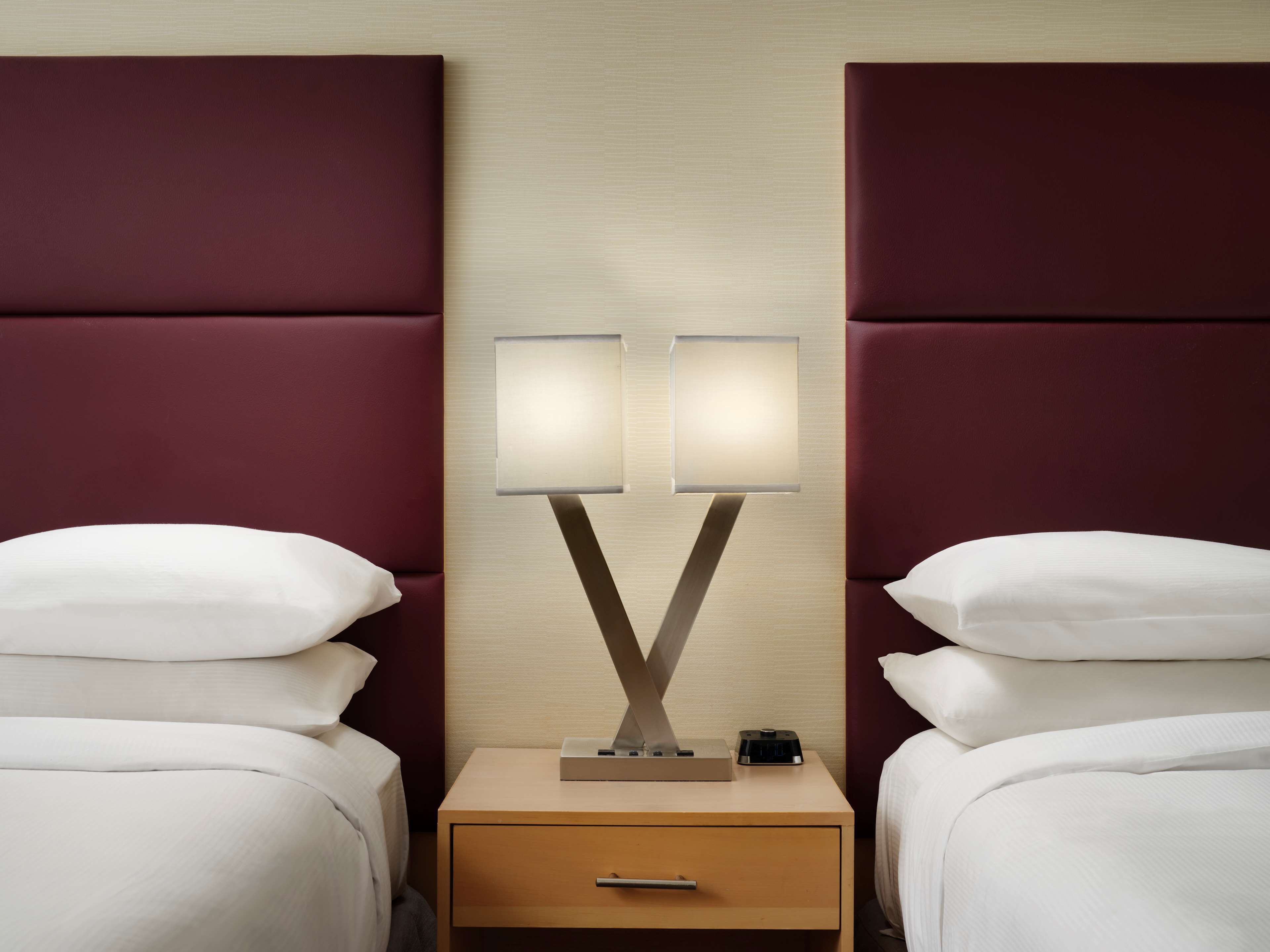A hotel room with two beds, a nightstand with a lamp, and a wooden drawer.