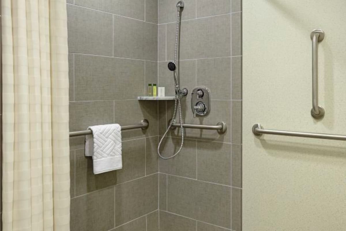 A shower area with a handheld showerhead, grab bars, and a towel rack.