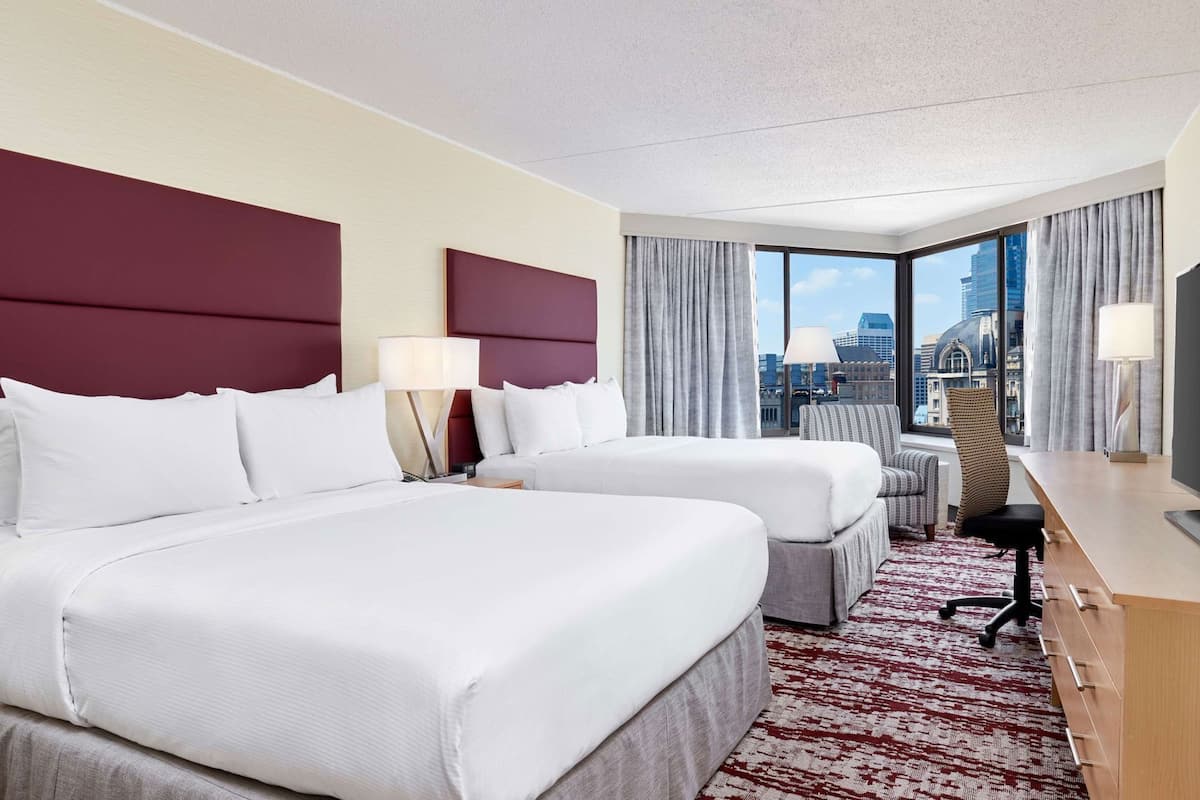 A hotel room with two beds, a desk, a chair, and a TV.